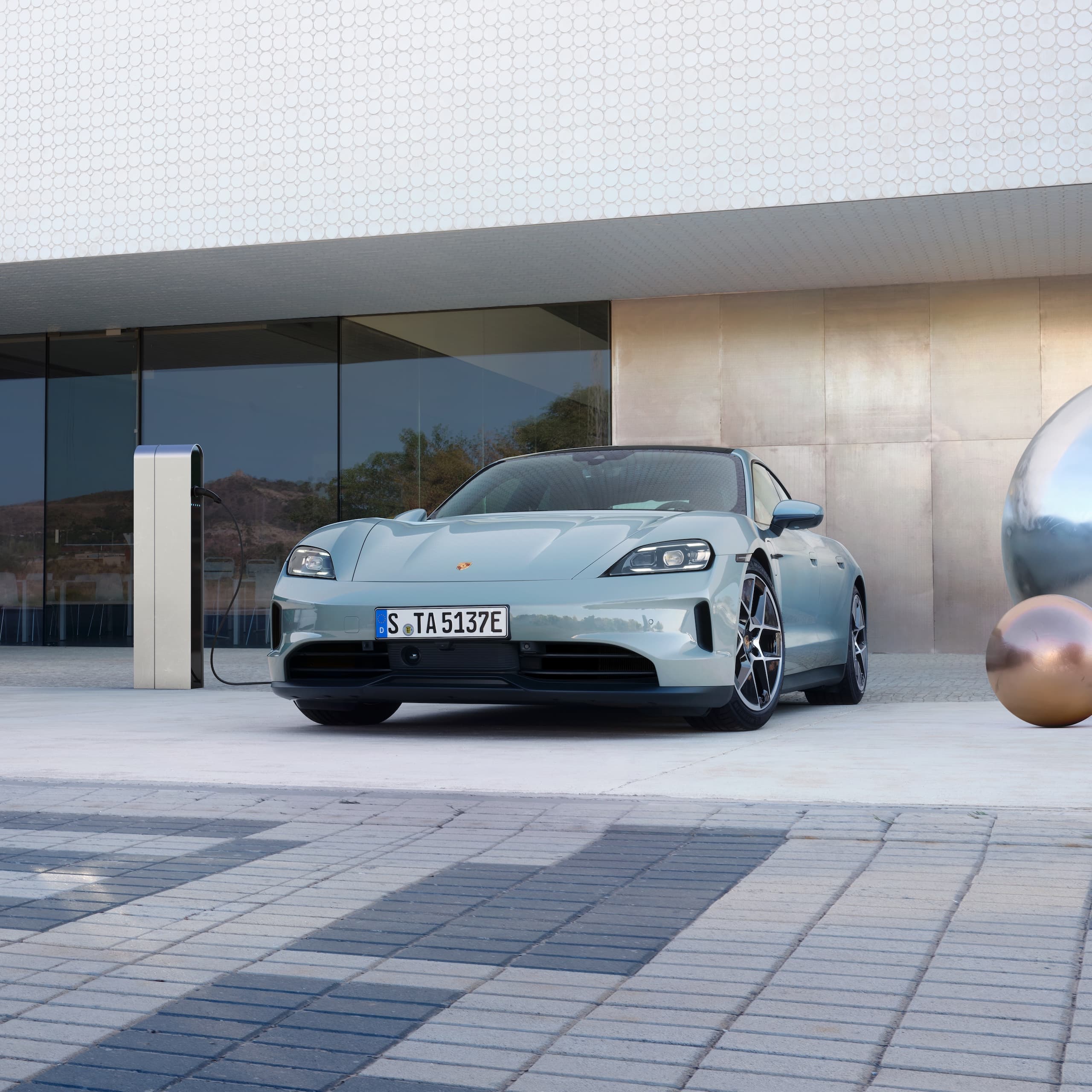Una Porsche Taycan parcheggiata fuori davanti a un edificio moderno.